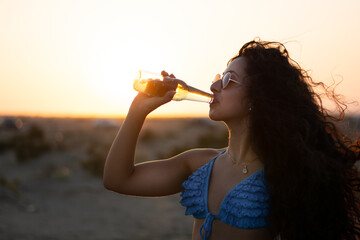 Woman drinking beer against sunset sky on summer beach holidays