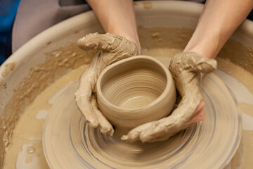 Woman working on the potter's wheel. Artisan making a cup from clay pot. Workshop of handmade modeling on the potters wheel.