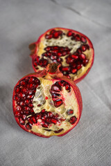 A red ripe pomegranate torn in half lies on a gray canvas