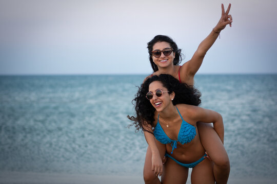 Women best friends having fun with piggyback ride on beach