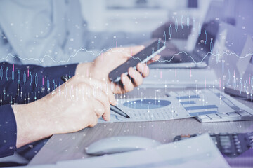 Double exposure of man's hands holding and using a digital device and forex graph drawing. Financial market concept.