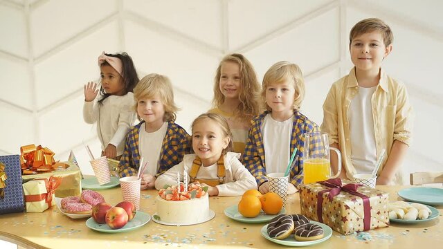 Children gathered at a festive table around the birthday girl, posing for a photographer taking memorable pictures.