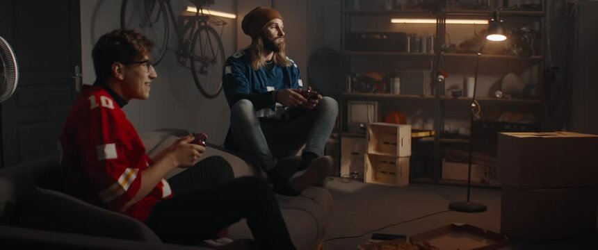 Portrait of two friends playing video game inside garage hideout, winning and celebrating. TV screen is not seen. Shot with 2x anamorphic lens