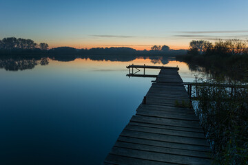 Fototapeta premium Wooden pier towards a calm lake and the sky after sunset