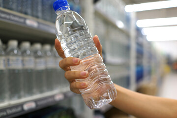 Close up female hand holding a bottle of drinking water in a grocery store.