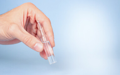 Medical ampoule in a man's hand on a blue background.