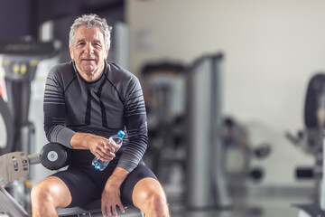Fototapeta na wymiar Pensioner keeps himself fit working out in a gym, resting with a bottle of water