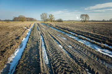 Muddy road with melting snow, plowed fields