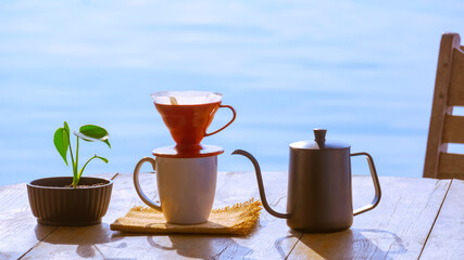 Drip coffee cup set with green plant in flower pot on wooden round table against riverside view background at morning time