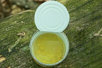 one open white tin can with canned corn in yellow water stands on a gray wooden board