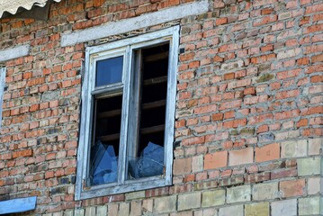 one old white window with broken glass on a red brick wall of a house on the street