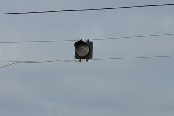 traffic light with one gray lamp on wires above the road against a  sky