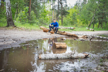 In the spring, in the forest near a large puddle, a boy Gibnik sits on a log, and there are baskets near him.