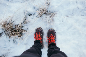 POV shot of woman look down on her brown leather winter boots with red laces stand in white winter snow. Winter wonderland hike. Frosty freezing temperatures, hiking in snow