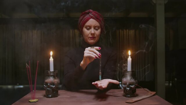 Senior woman fortune teller uses a blue magic crystal to future telling ritual