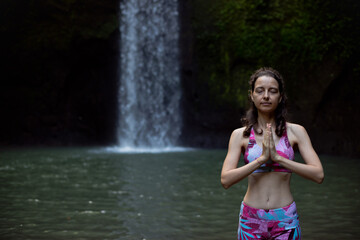 Close up of namaste mudra. Woman meditating, practicing yoga and pranayama with namaste mudra near waterfall. Yoga outdoor concept. Tibumana waterfall, Bali. Copy space.