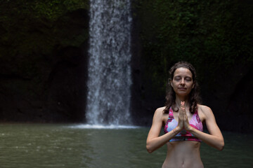 Close up of namaste mudra. Woman meditating, practicing yoga and pranayama with namaste mudra near waterfall. Yoga outdoor concept. Tibumana waterfall, Bali. Copy space.