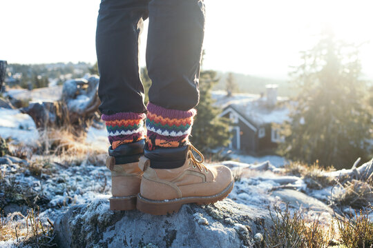 Male legs in black pants and hand knitted wool traditional ornament socks, leather suede winter boots or hiking shoes. Man on cold frosty mountain walk in snow in scandinavia