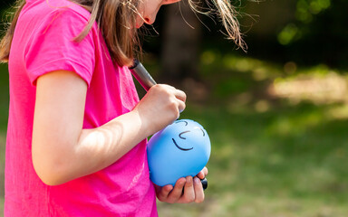 Young child, sa little girl drawing a happy smiling face on a ballon using a black marker outdoors, closeup. Children and imaginary friends, loneliness, creative arts and crafts ideas abstract concept