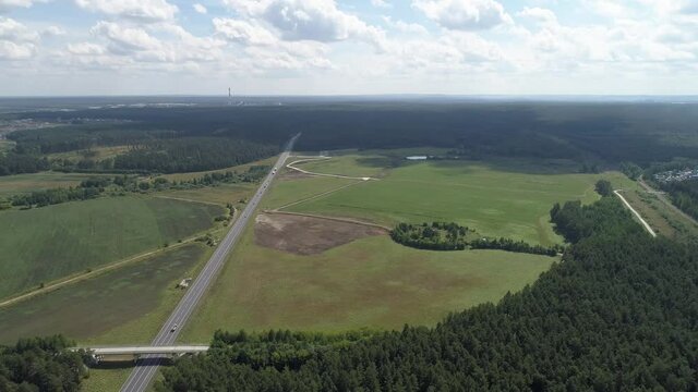 Aerial view of highway with cars. Nearby forests and fields. Nearby is a plot for the construction of an industrial facility with convenient access to the highway. Summer sunny day
