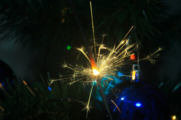 lit Sparkler on the background of a Christmas tree with toys on Christmas day.