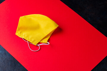 Face protective mask on a dark background. Yellow face mask on red paper. Reusable antivirus mask. Pop art style. Copy space