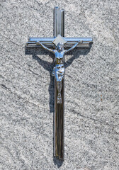 Shiny silver metal Christian cross, crucifix in the sun on grave stone background. Christian...