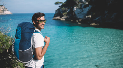 South Asian hipster guy wanderlust with rucksack enjoying summer vacations for explore wild nature at coastline, Indian male enjoying travel active recreating during solo holidays on Balearic islands © BullRun