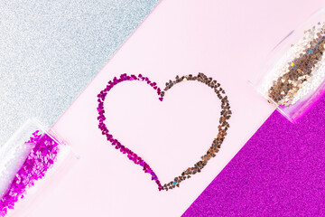 Heart shape made of multicolored glitter. Two champagne glasses with splash of heart shaped confetti over glitter background. Valentine's Day concept. Copy space. Top view