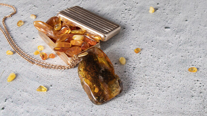 Dazzling big  Baltic yellow and green  amber pendant with the inclusion of an ancient plant and moss  and old metal box with pieces of natural amber on the gray plastered background. 