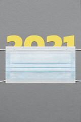 Figure 2021 under a blue face mask on a dark paper textured background. Composition using the pantone's colors of the year.