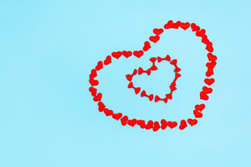 Heart-shaped frame made of confetti and bows on a blue background. The background of Valentine's day. flatly, top view, copy space