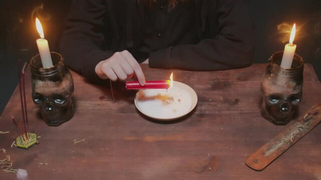 Close up of young witch female fortune teller holds candle which dripping wax into a plate to makes cross in terrible magic ritual
