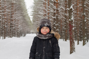 Fototapeta na wymiar European boy in the forest in a hat in winter on the background of snow.