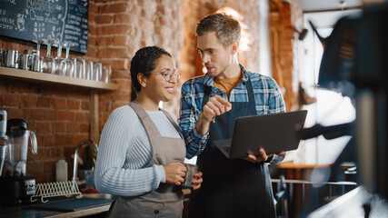 Two Diverse Entrepreneurs Have a Team Meeting in Their Stylish Coffee Shop. Barista and Cafe Owner Discuss Work Schedule and Menu on Laptop Computer. Multiethnic Female and Male Restaurant Employees.