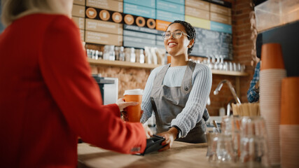 Joyful Multiethnic Diverse Woman Gives a Payment Terminal to Customer Using NFC Technology on...