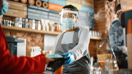 Mandatory Face Masks and Shields in a Coffee Shop During Coronavirus Pandemic. Female Customer Pays for Coffee and Pastry with Contactless NFC Payment Technology on Smartphone to a Barista in Cafe.