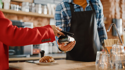 Close Up of a Feminine Hand Holding a Smartphone with an NFC Payment Technology Used for Paying for Croissant in a Cafe. Customer Uses Mobile to Pay for Latte Through a Credit Card Terminal.