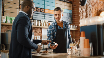African American Customer Pays for Coffee and Pastry with Contactless NFC Payment Technology on Smartphone to a Handsome Barista in Blue Checkered Shirt. Contactless Mobile Payment in Cafe Concept.