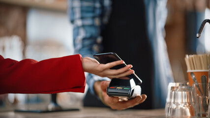 Close Up of a Feminine Hand Holding a Smartphone with an NFC Payment Technology Used for Paying for Take Away Coffee in a Cafe. Customer Uses Mobile to Pay for Latte Through a Credit Card Terminal.