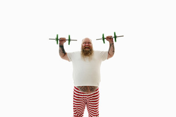 Isolated portrait of an overweigh bearded man with tattooed arms exercising with dumbbells and having fun looking at camera