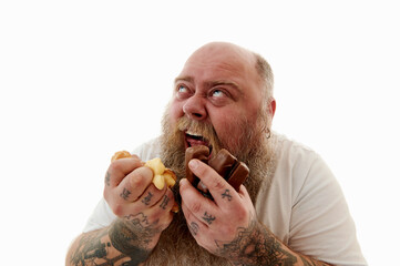 Portrait of an obese man squeezing eclairs and chocolate bars into his fists thereby expressing...