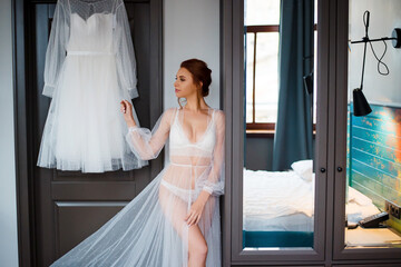 Gorgeous bride in lace lingerie standing near wedding dress