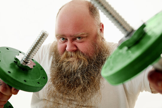 Close up of an overweigh bearded man looking sternly at camera and imange of dumbbells on the foreground. Isolated on a white background