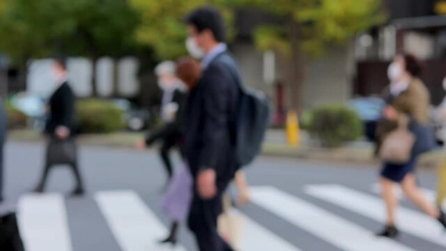 意図的にピントをぼかした東京駅前の横断歩道を渡るマスク姿のビジネスマンたちのスローモーション動画