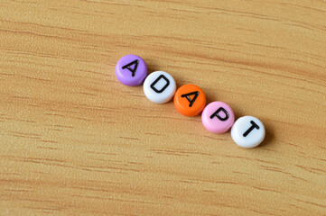 Selective focus of colorful alphabet beads with text ADAPT over wooden background
