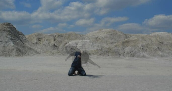 Lonely exhausted traveler goes mad in  desert. Long-haired man in dirty clothes dancing crazy dance on sand kneeling and raising hands 4k slow motion 50 fps