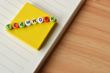 Selective focus with blurred effect of notebook, wooden blocks and colorful alphabet beads with text TEAMWORK. Business and education concept. 