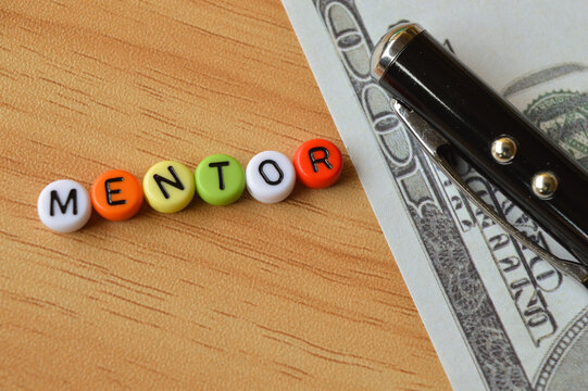 Selective focus of pen, money banknote and colorful alphabet beads with text MENTOR. Business concept. 