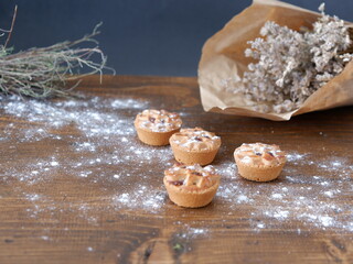 The snack pies are on the table. The little pies prepared for the New Year come out of the frill. The pies are sprinkled with powdered sugar on them. The pie prepared on a wooden table.